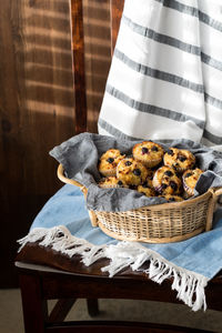 A basket filled with homemade blueberry muffins, on a wooden chair.