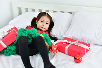 Portrait of cute girl lying with christmas gift and decoration in bed at home