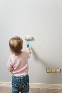 Little child painting the wall with roller in the empty room, grey background. interior decoration