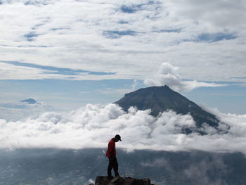 Hiker standing on mountain against cloudy sky