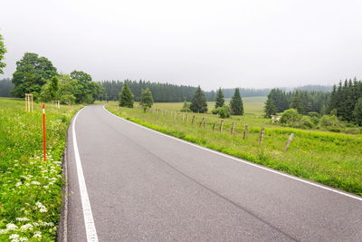 Empty road along landscape and trees against sky