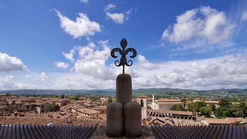 Cross on street amidst buildings against sky