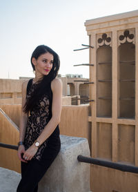 Portrait of young woman standing by railing against clear sky