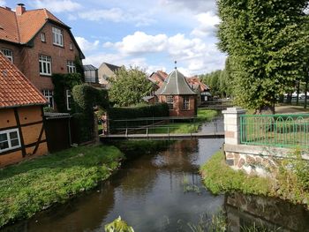 Canal amidst houses and trees against sky