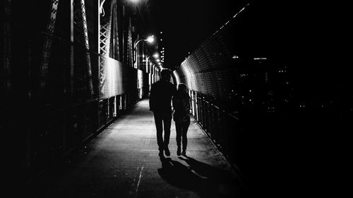 Rear view full length of couple walking on manhattan bridge at night