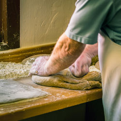 Midsection of man kneading dough in bakery