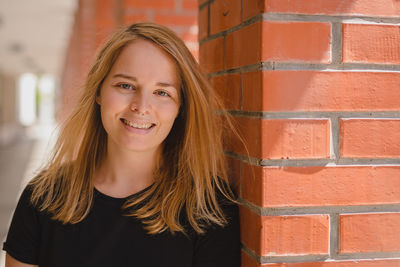 Portrait of smiling beautiful woman with blond hair standing by architectural column