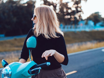 Cheerful young woman wearing sunglasses sitting on motor scooter