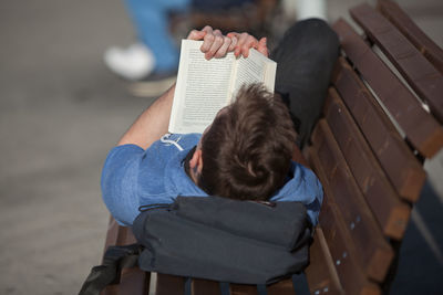 Man reading book while lying on bench at footpath