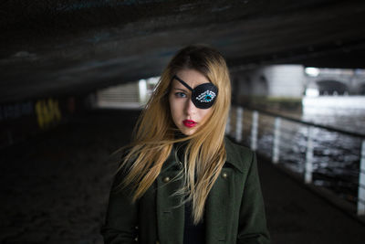 Portrait of young woman wearing costume eye patch below bridge