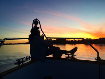 Silhouette man sitting on boat against sky during sunset