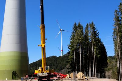 Construction machine by windmills on field against clear blue sky