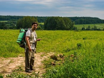 Full length of backpack male hiker standing on grassy field