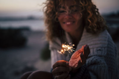 Portrait of smiling woman holding sparkler outdoors