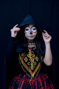 Portrait of woman holding camera while standing against black background