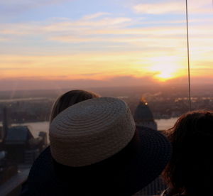 Rear view of woman looking at cityscape against sky during sunset