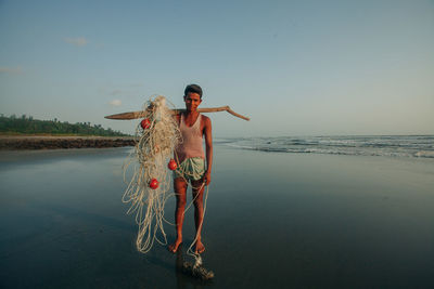 Man with fishing net standing at beach against sky