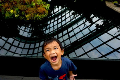 Close-up portrait of boy shouting while standing against pond