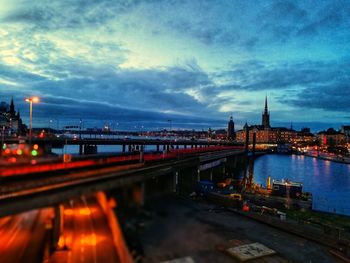 Illuminated bridge over river against cloudy sky
