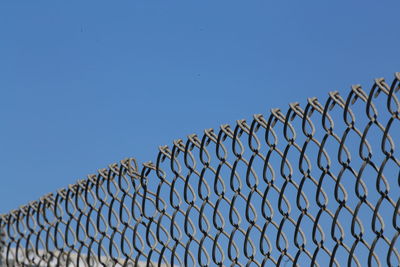 Low angle view of chainlink fence against clear blue sky