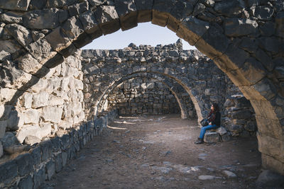 Full length of woman sitting by stone wall