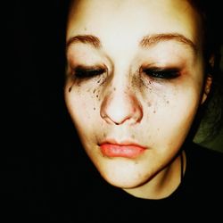 Close-up of sad young woman crying against black background