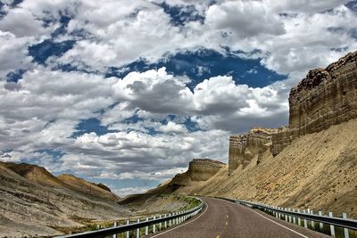 Empty road by cliff against cloudy sky