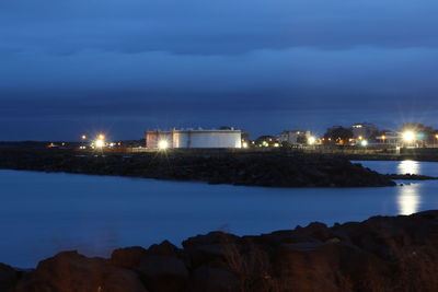 Illuminated buildings by sea against sky at night