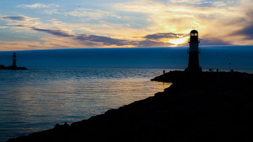 Silhouette lighthouse by sea against sky during sunset