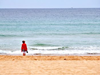 Rear view of man standing on beach against sky