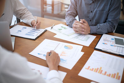 Midsection of business people working on graphs on table in office