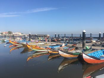 Boats moored at harbor against blue sky