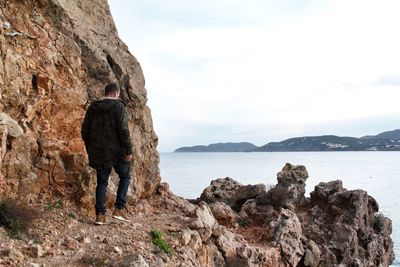 Rear view of man walking on rock formation at sea against sky