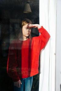 Girl looking away while standing on window sill