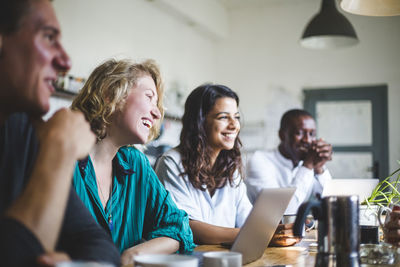 Smiling professional hackers looking away while sitting at table in start-up office