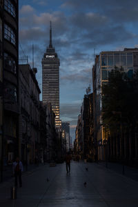 People walking in city against cloudy sky