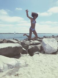 Full length of teenage girl jumping at beach against sky during summer