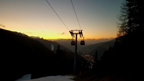 Low angle view of ski lift by mountains against sky during sunset