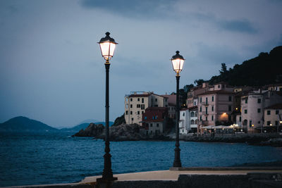 Illuminated street light by building against sky