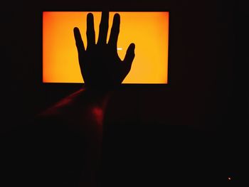 Close-up of silhouette hand on illuminated lamp