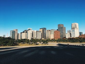 Road by buildings against clear blue sky