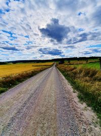 Country road amidst field against sky