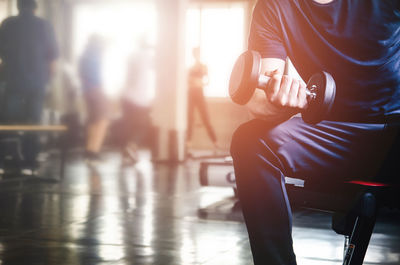 Midsection of man lifting dumbbell in gym