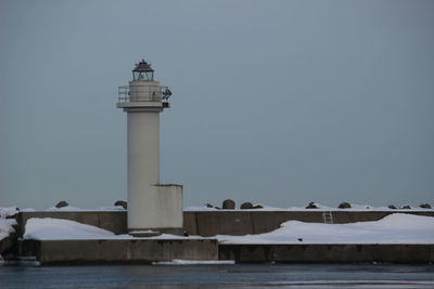 Lighthouse by sea against clear sky