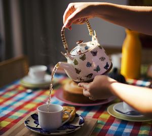 Cropped hands pouring tea in cup on dining table at home