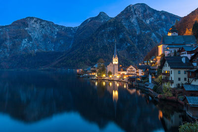 Lake by illuminated buildings against sky at dusk