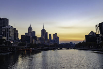 River by buildings against sky during sunset