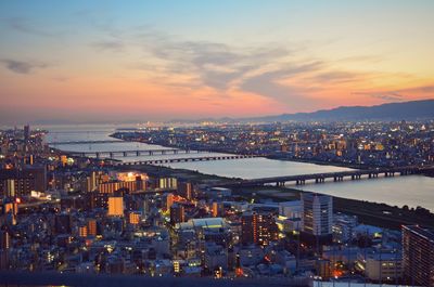 High angle view of illuminated city by river at sunset