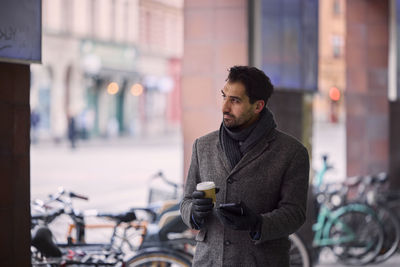 Elegant man with smartphone and paper cup on street