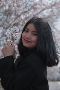 Portrait of smiling young woman standing by flowering plants